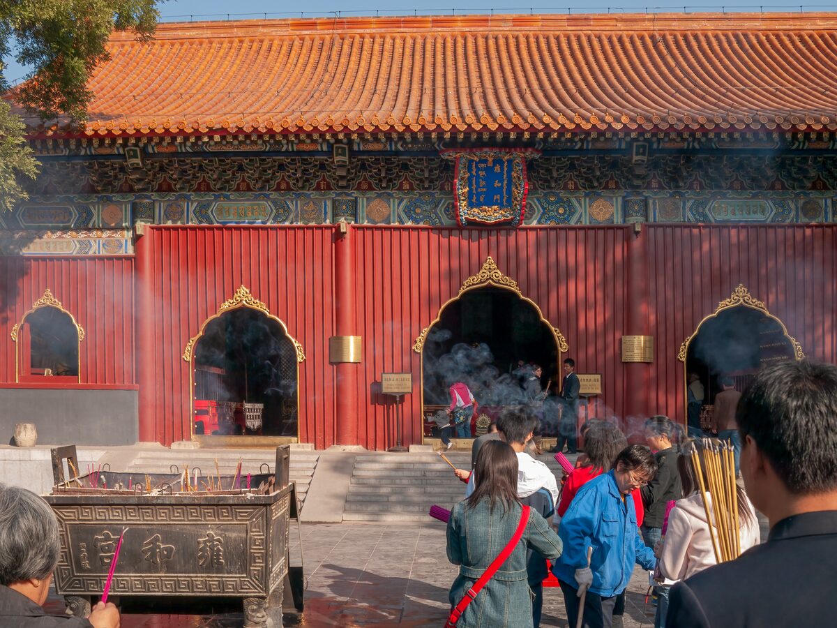 The Hall of the Heavenly Kings at Yonghe Temple, a red hall with an orange-tiled roof, incense smoke and worshippers in the courtyard in front