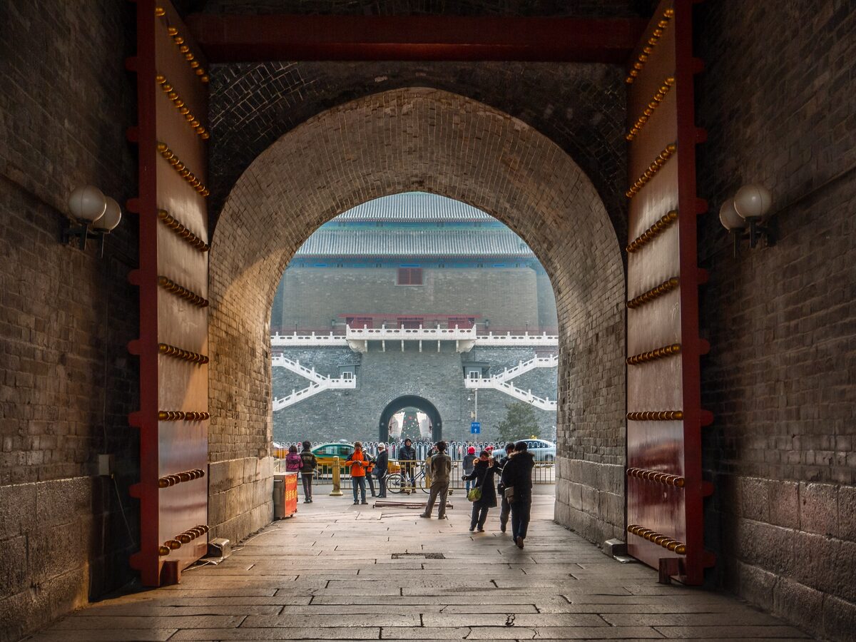Looking through the brick arch of the Zhengyangmen gate to the Arrow Tower beyond, with visitors walking the passage