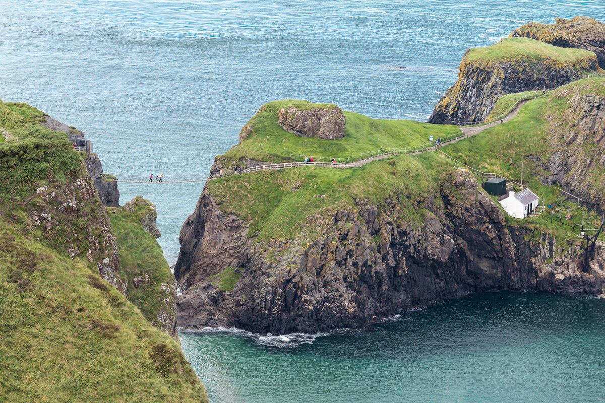 Carrick-a-Rede, a small rocky island with green grass joined to the cliffs by a narrow rope bridge over turquoise water