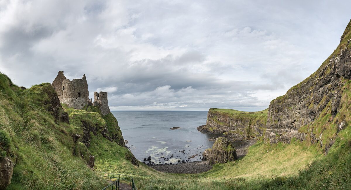 The ruins of Dunluce Castle on the edge of a cliff above the sea, framed by green hillsides