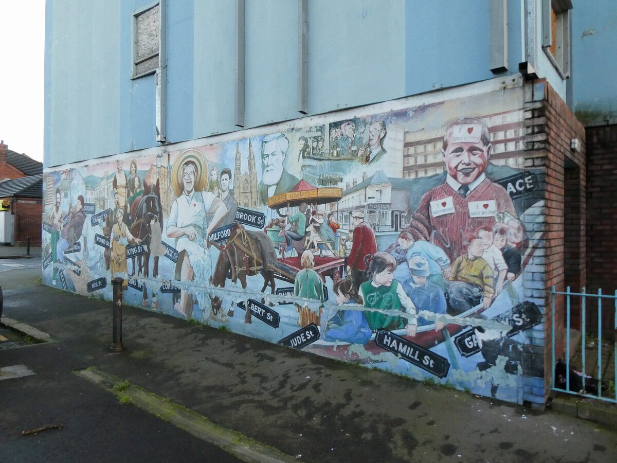 A large colorful community mural painted on the side of a building on a street in Belfast