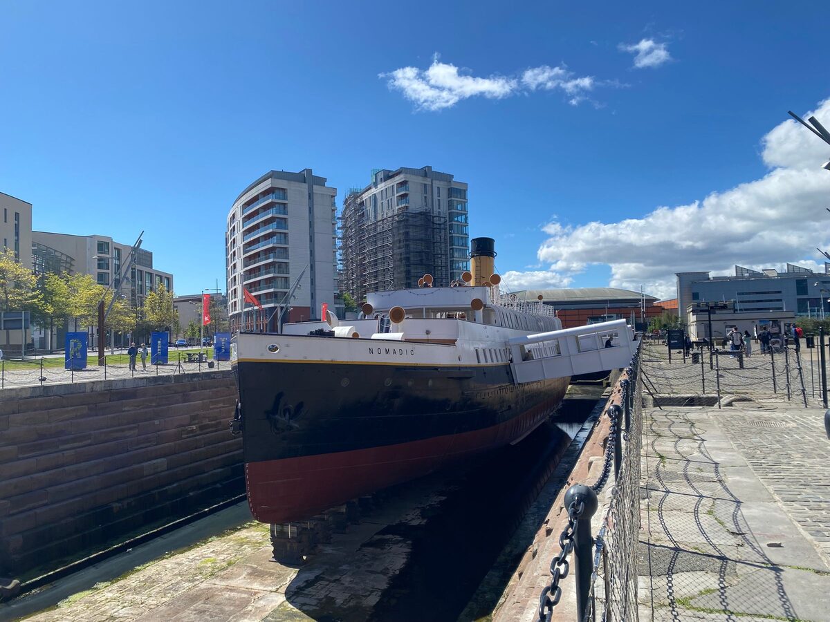 The SS Nomadic, a small black-and-white steamship with a tall funnel, in its dry dock in the Titanic Quarter