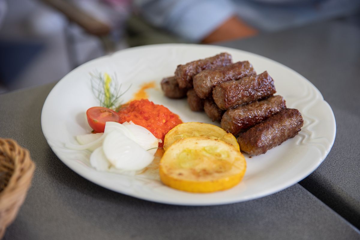 A plate of grilled ćevapi with ajvar, raw onion and grilled zucchini