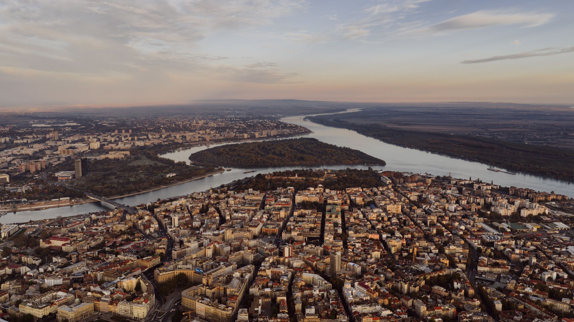Aerial view of Belgrade at dusk, with the old town and Kalemegdan in front and Great War Island where the Sava meets the Danube