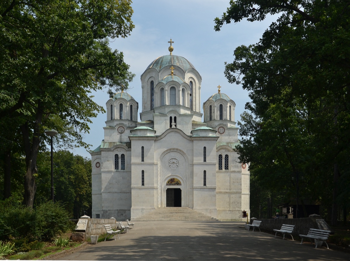 The white marble Church of St. George at Oplenac with its green domes, at the end of a tree-lined path
