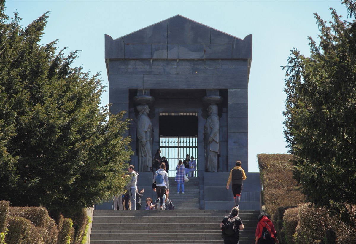 Visitors climbing the steps to the Monument to the Unknown Hero, a black granite tomb with two stone caryatids at its entrance