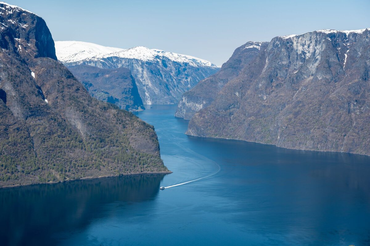 The deep blue Aurlandsfjord between steep green mountainsides with snow on the peaks, seen from high above