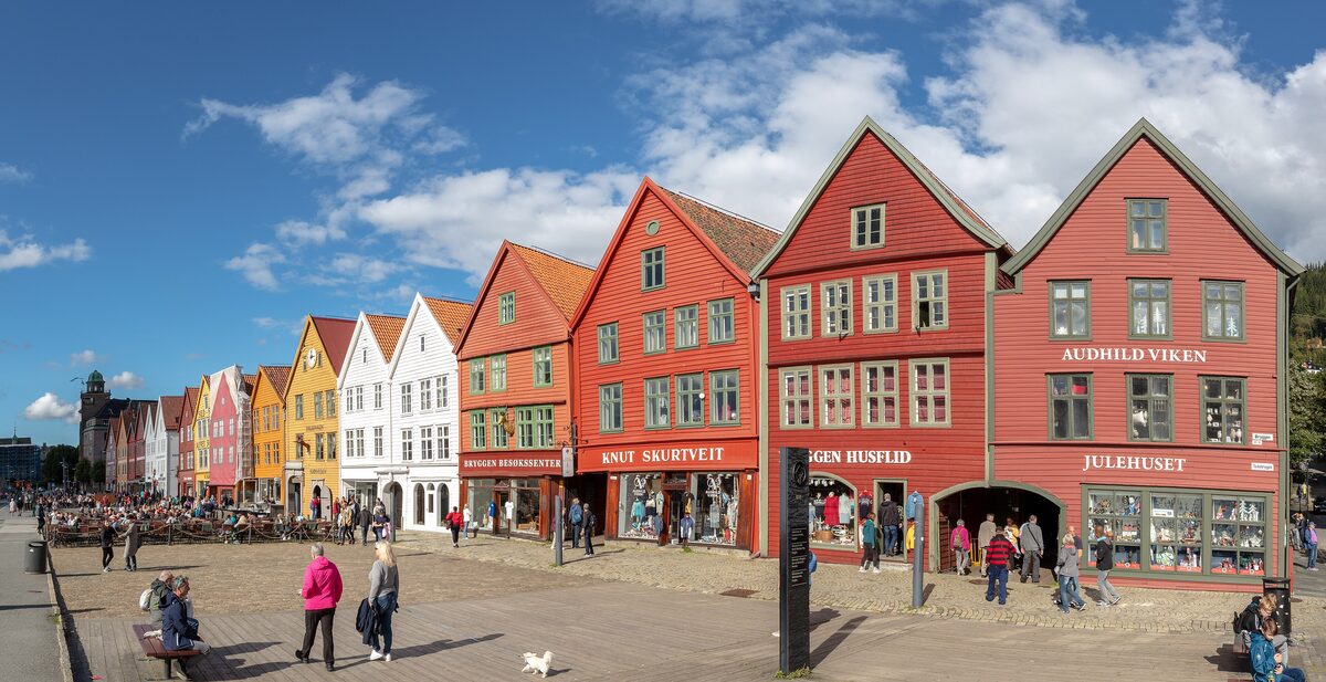 The row of red, yellow and white wooden gabled houses of Bryggen along the harbor in Bergen, under a blue sky