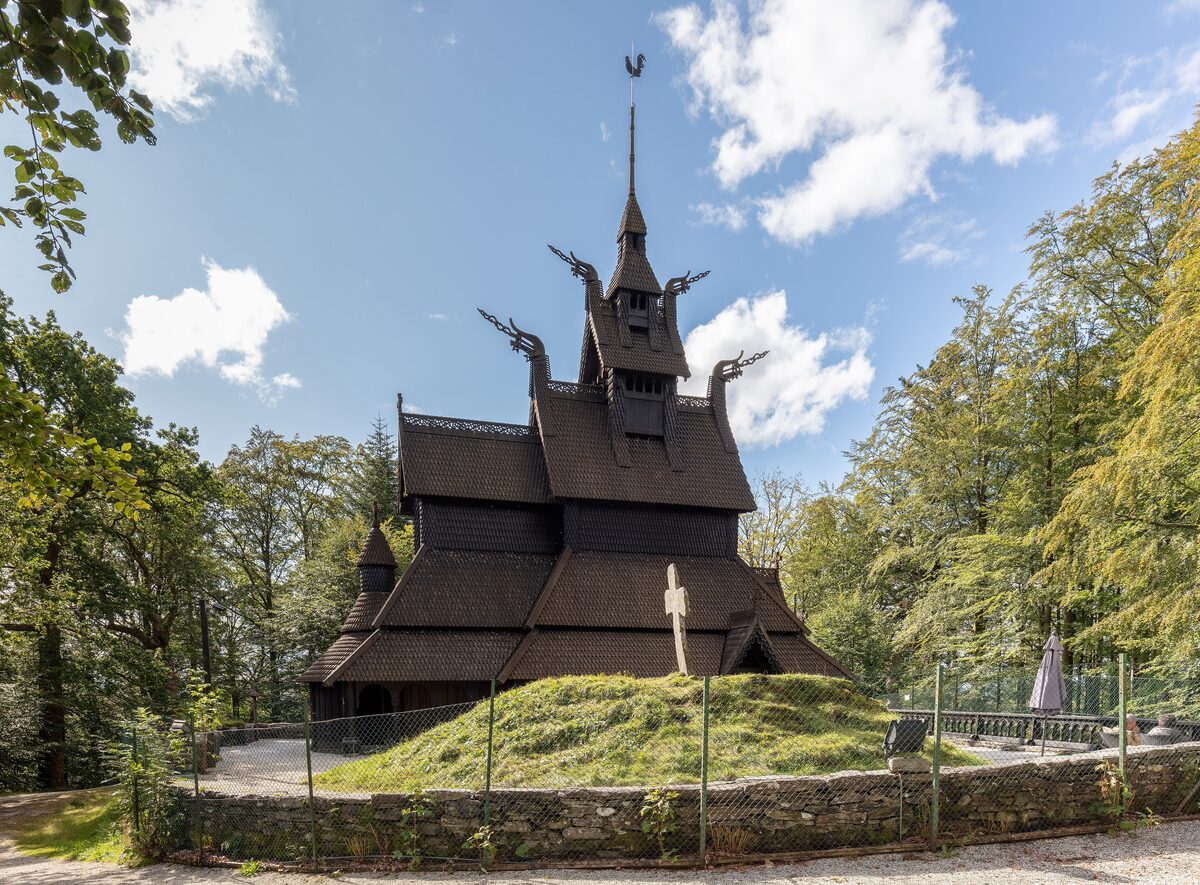 The dark wooden Fantoft stave church with dragon heads on its stacked roofs, among green trees