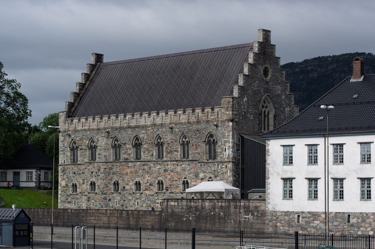 The grey stone medieval Håkonshallen with its stepped gable and Gothic windows, next to a white building at Bergenhus