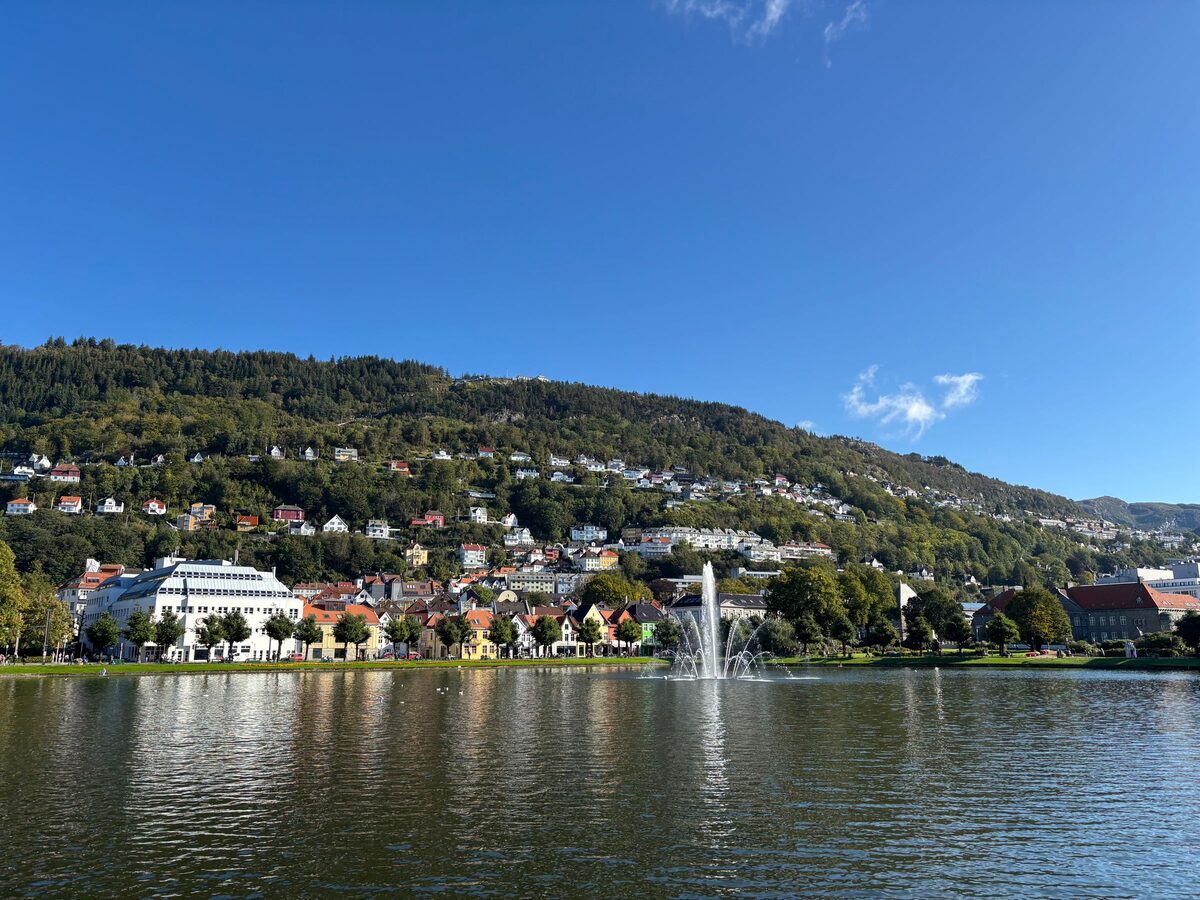 The lake Lille Lungegårdsvann in central Bergen with a fountain, a white building on the far shore and houses on the green hillside