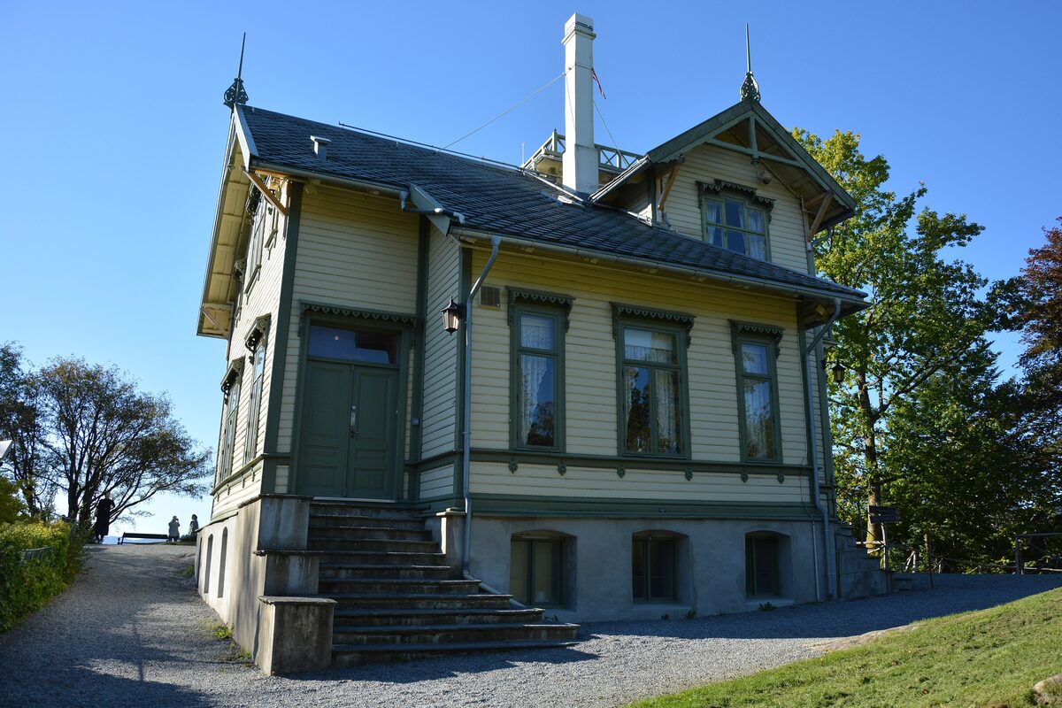 Edvard Grieg's yellow wooden villa at Troldhaugen with a green veranda and stairs, under a blue sky