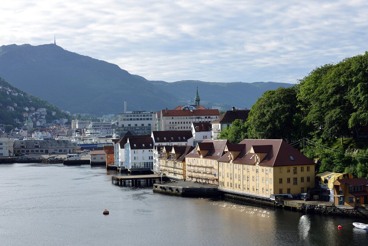 The green mountain Ulriken with its antenna on top, rising behind Bergen's harbor and yellow waterfront buildings