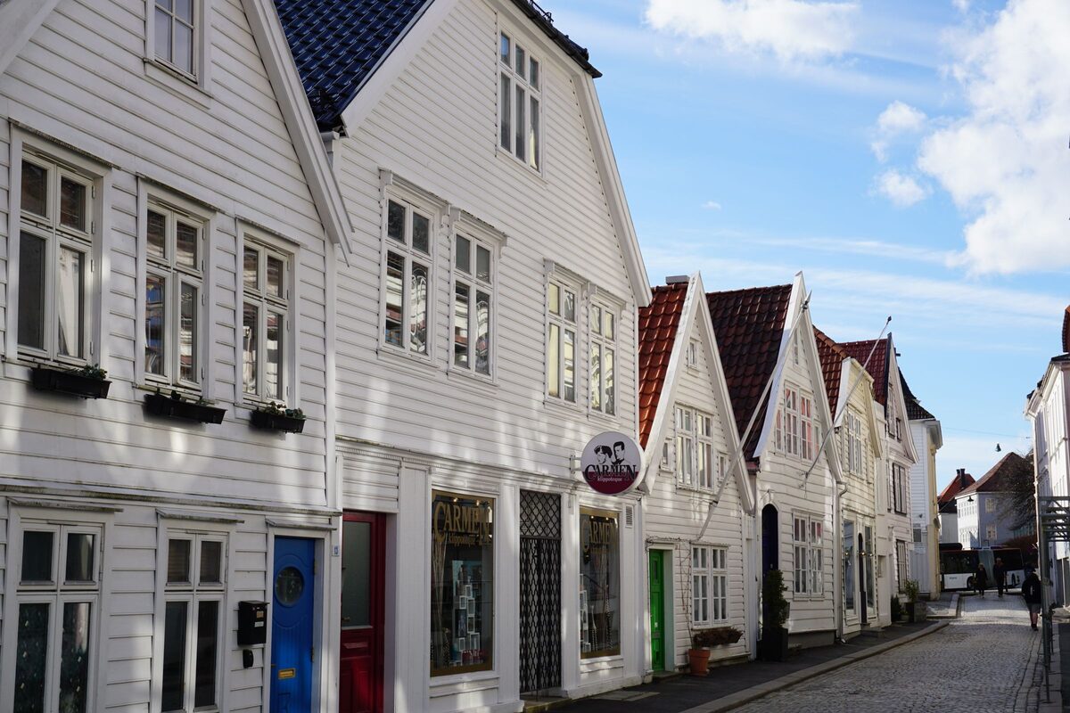 A row of white wooden houses with colorful doors and window boxes along a quiet street in Bergen