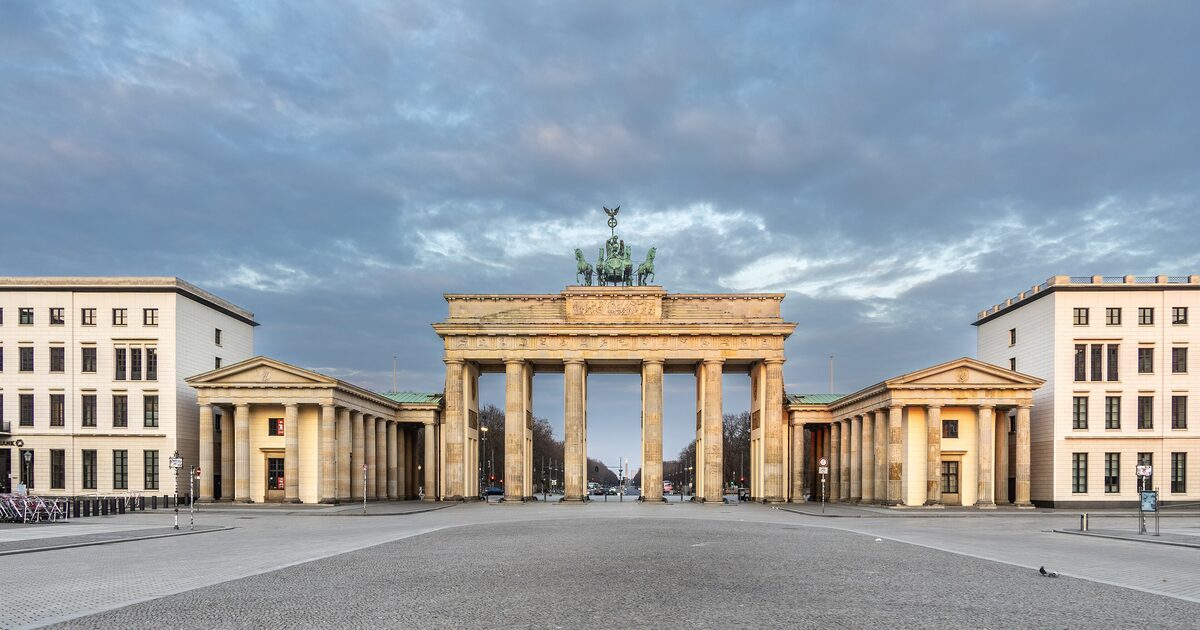 The Brandenburg Gate in Berlin at dawn, with the bronze chariot on top and an empty Pariser Platz in front under a cloudy sky