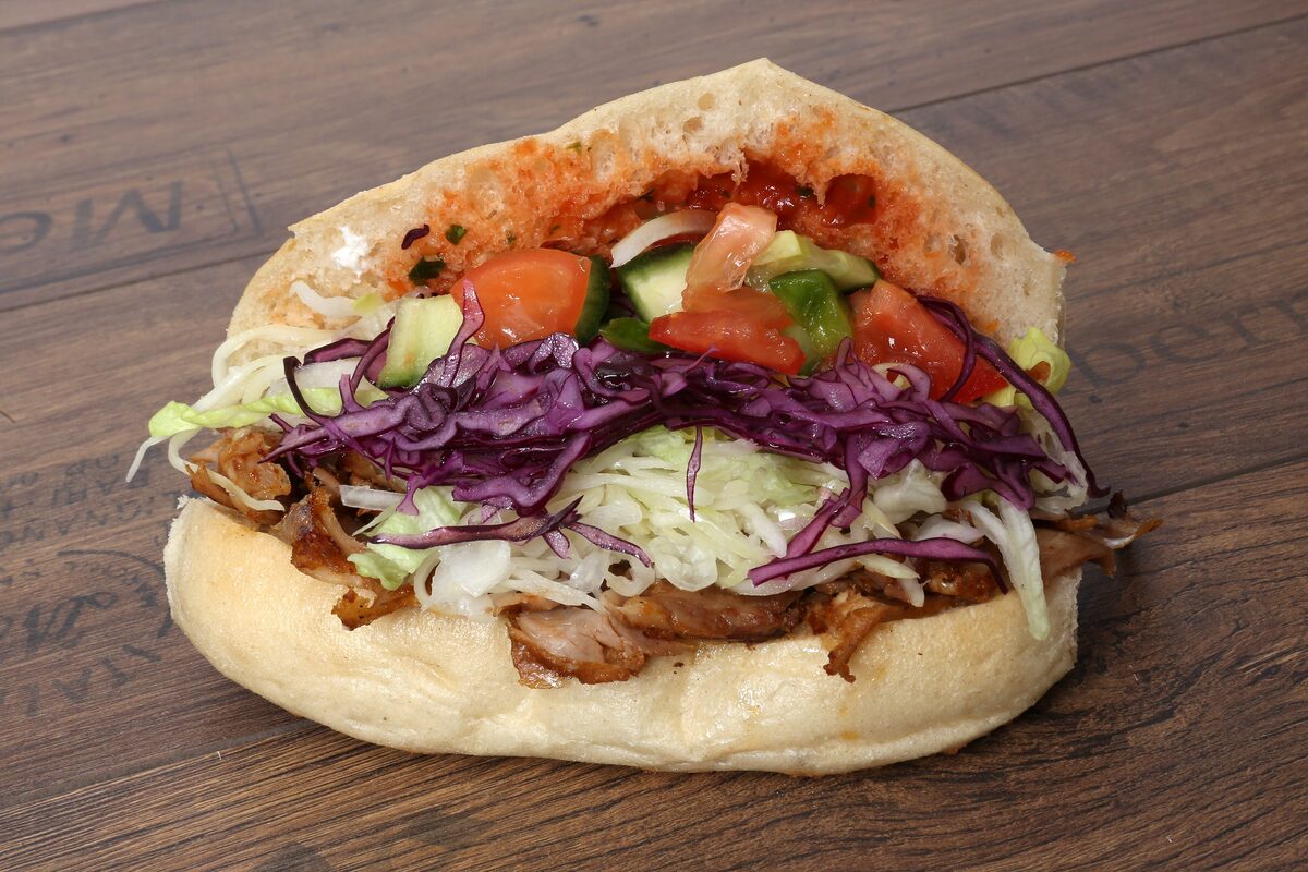 A döner kebab sandwich in flatbread, filled with shaved meat, cabbage, cucumber, tomato and sauce