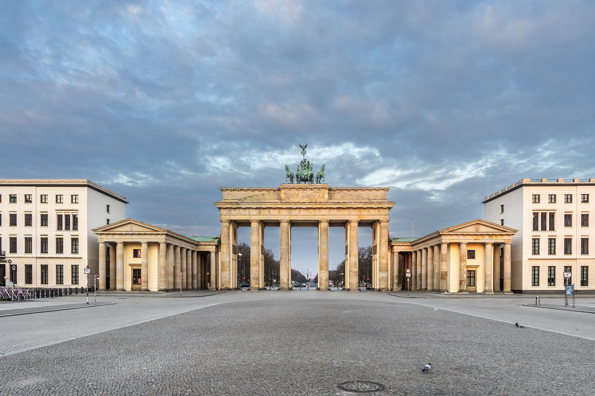The Brandenburg Gate in Berlin at dawn, with the bronze chariot on top and an empty Pariser Platz in front under a cloudy sky