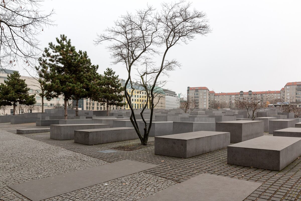 Grey concrete slabs of different heights at the Memorial to the Murdered Jews of Europe, with bare and pine trees and apartment blocks beyond