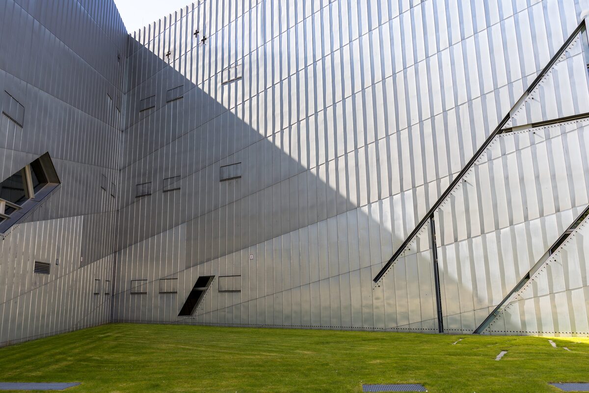 The zinc-clad wall of Daniel Libeskind's building at the Jewish Museum Berlin, with narrow diagonal window slits above a lawn
