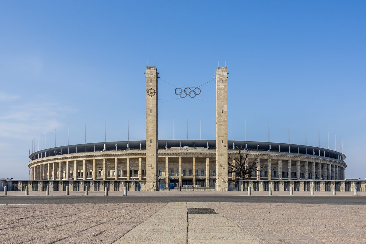 The Olympiastadion behind its two towers with the Olympic rings hanging between them, across a wide paved forecourt