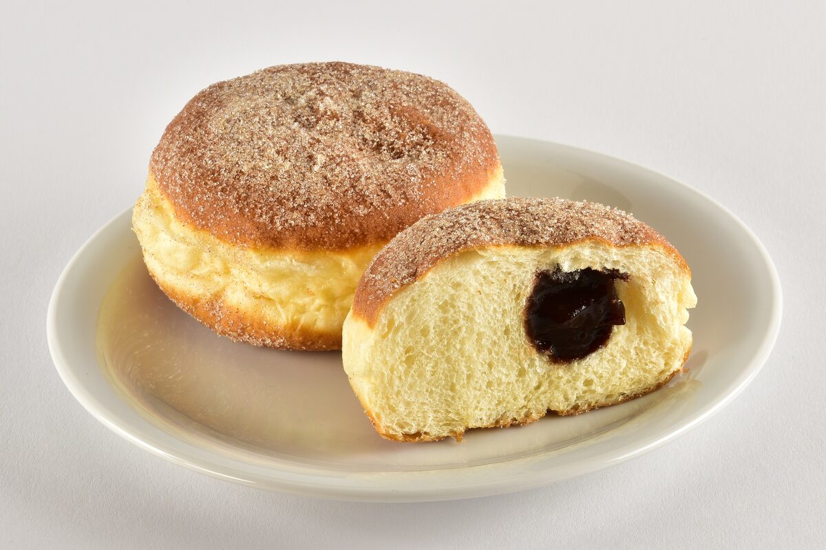 A Berliner Pfannkuchen, a sugar-dusted doughnut, whole and cut open to show the dark jam filling
