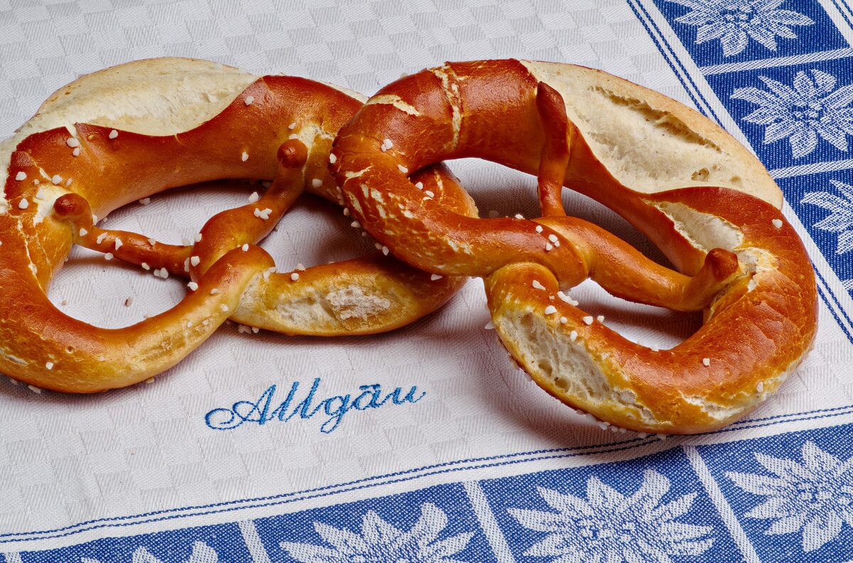 Two golden-brown pretzels with coarse salt on an embroidered cloth