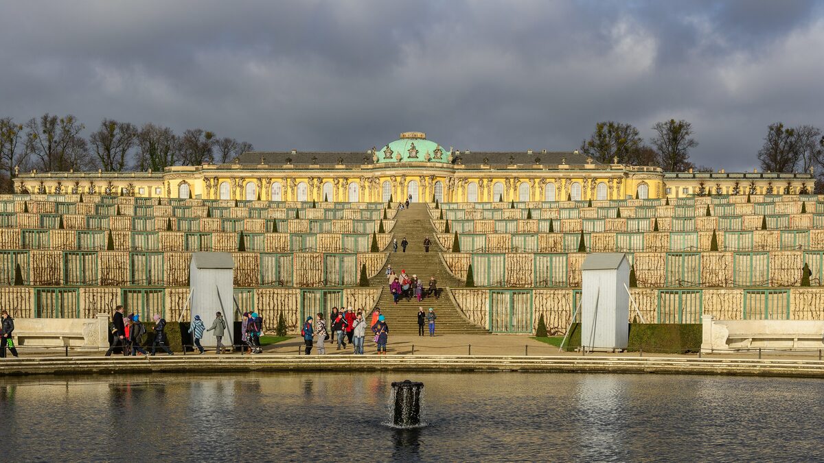 Sanssouci Palace on top of its vineyard terraces, seen across a fountain pond under a dark autumn sky