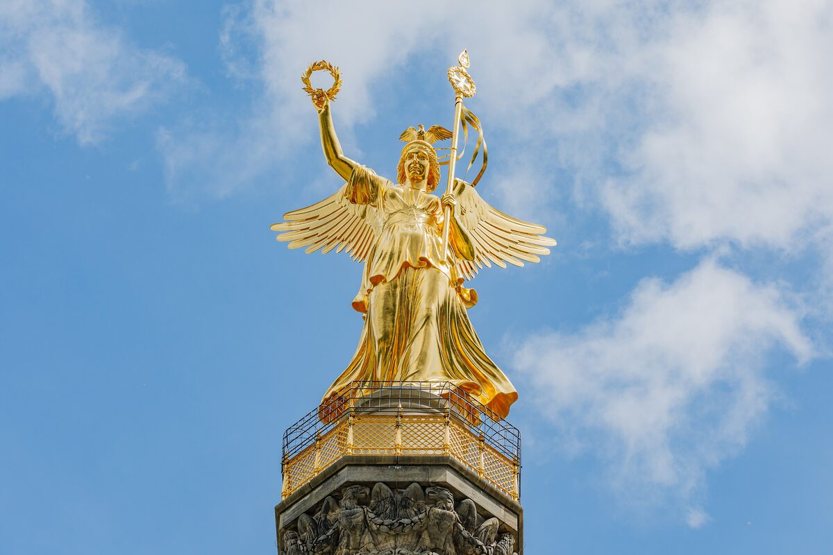 The golden statue of Victoria on top of the Victory Column against a blue sky with a few clouds