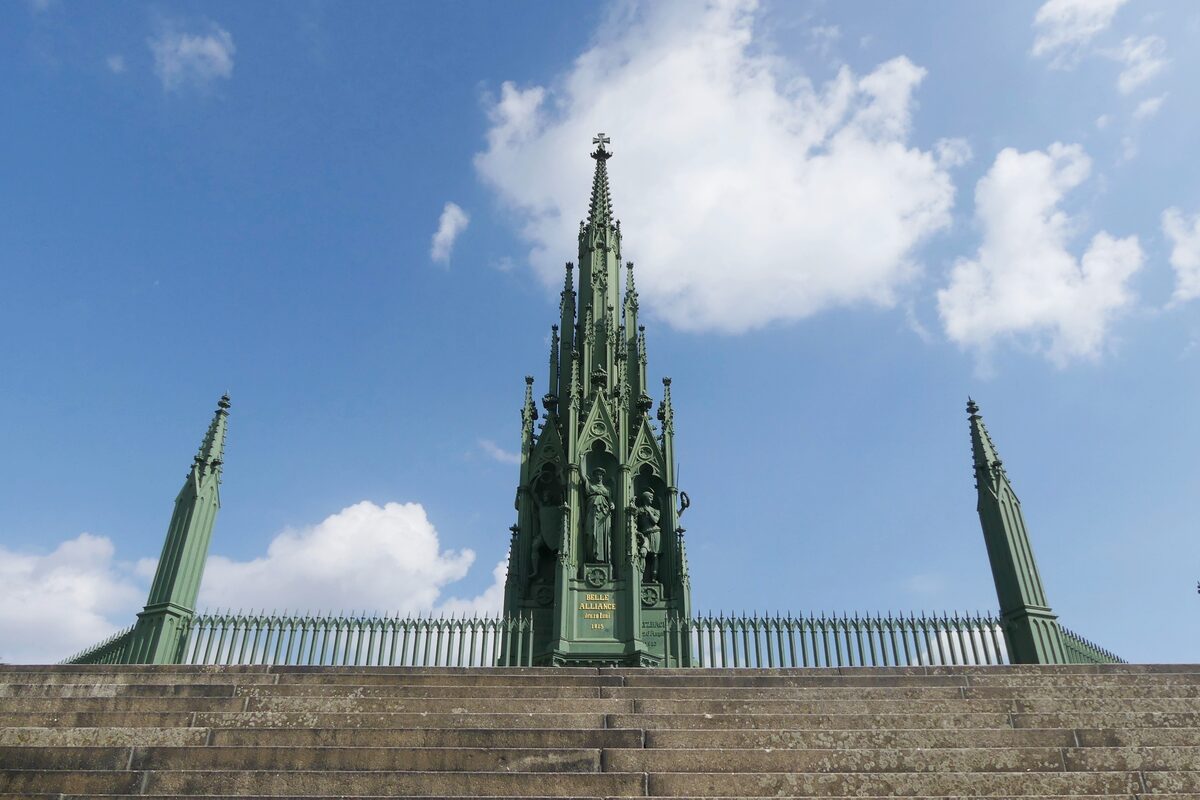 The green cast-iron National Monument at the top of Viktoriapark, seen from the foot of its steps against a blue sky