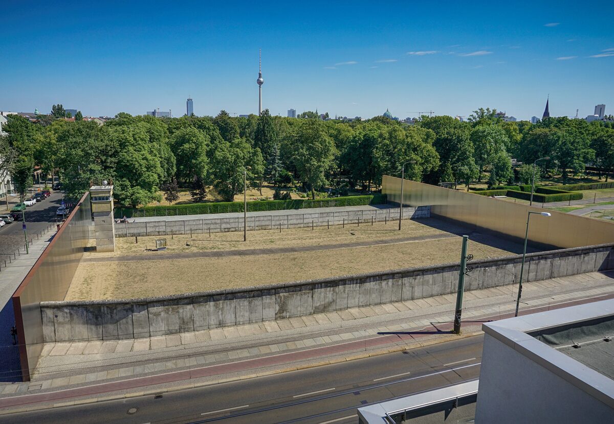 A preserved stretch of the Berlin Wall and the open death strip at the Bernauer Straße memorial, with the TV Tower on the horizon