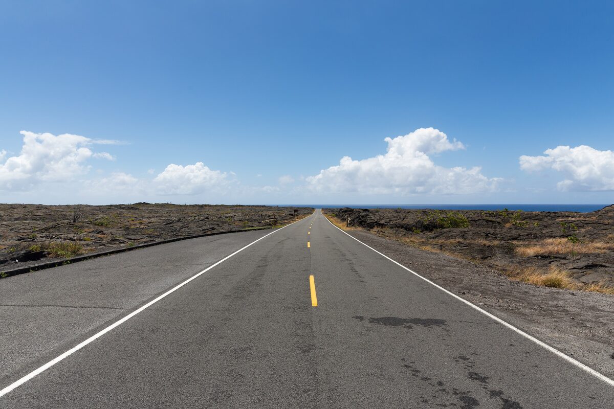 A straight road crossing black lava toward the sea