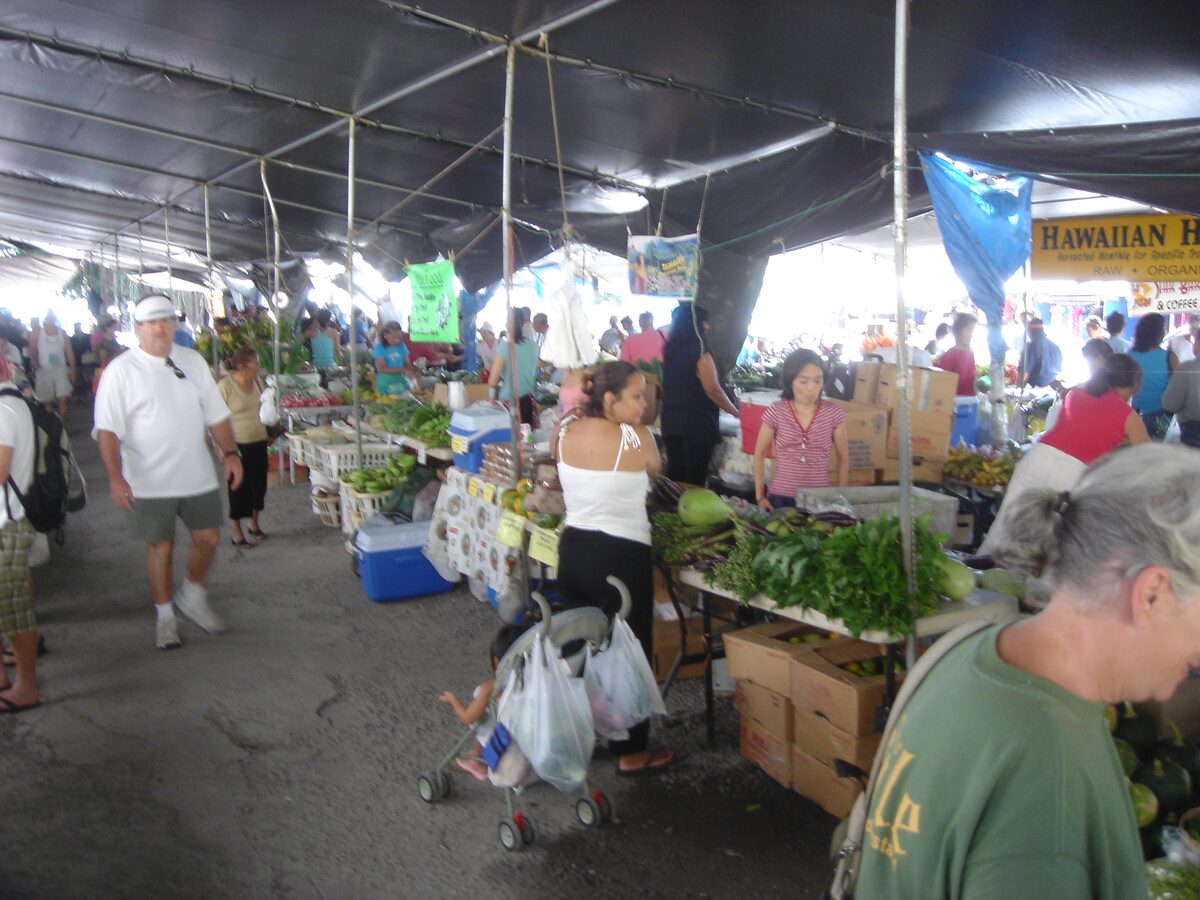 Shoppers and vegetable stalls under tents at Hilo's farmers market