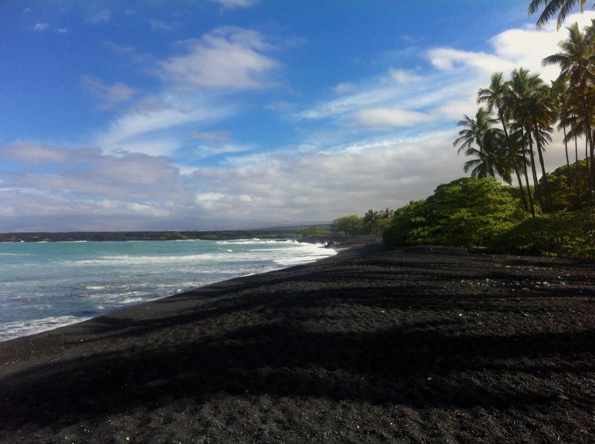 Black sand shore and palm trees at Kīholo Bay