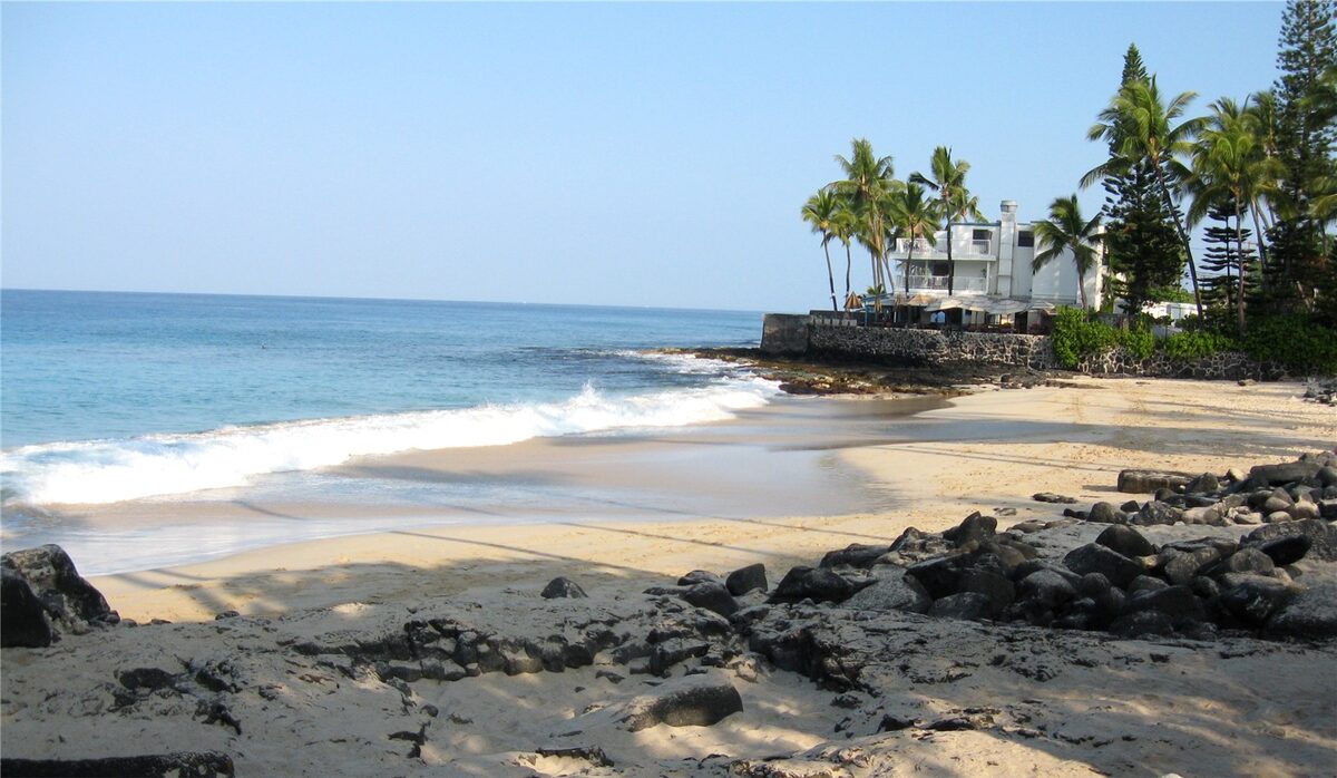 Sandy Kona cove with surf, lava rocks and palm trees