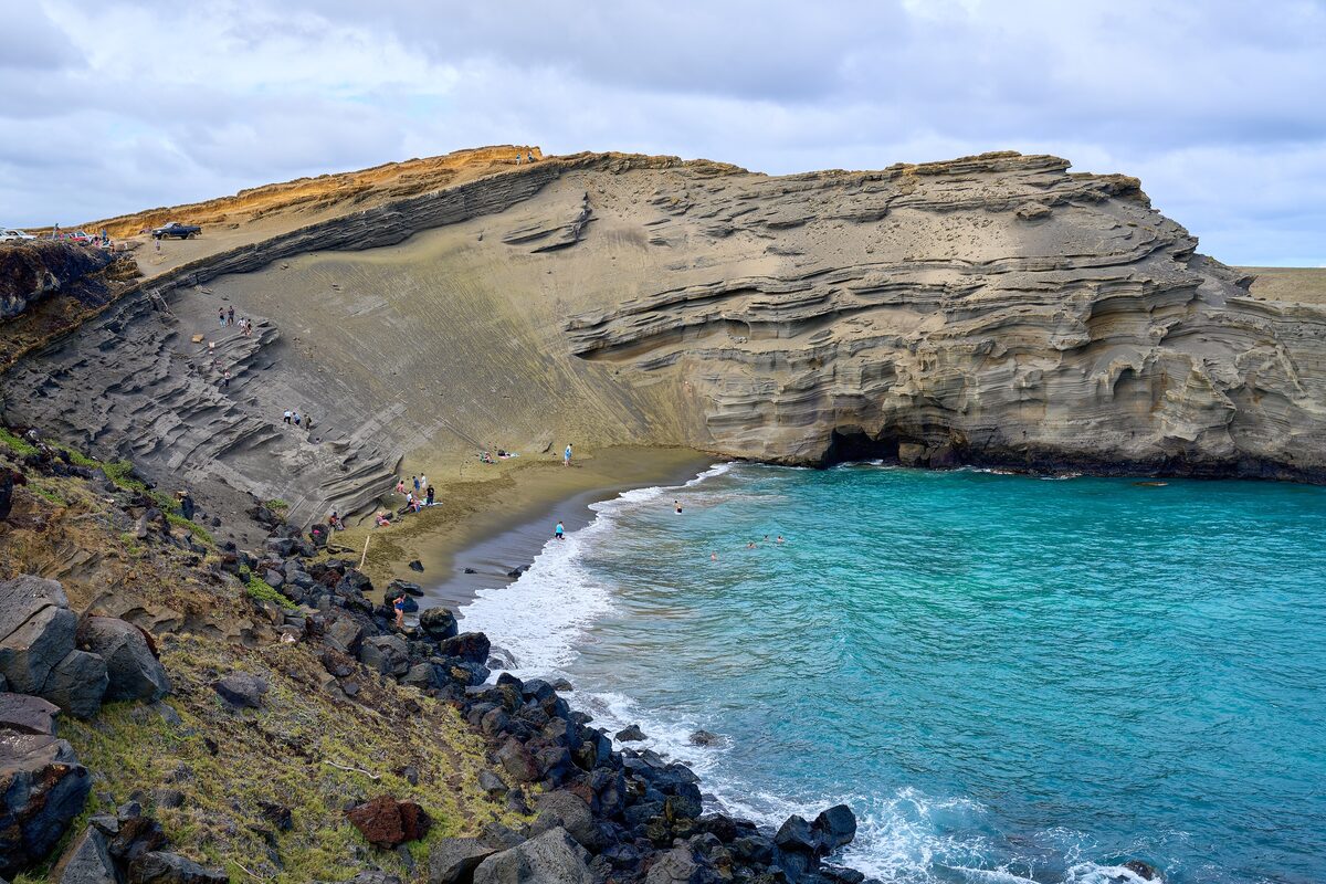 Turquoise bay below olive-green cliffs at Papakōlea beach