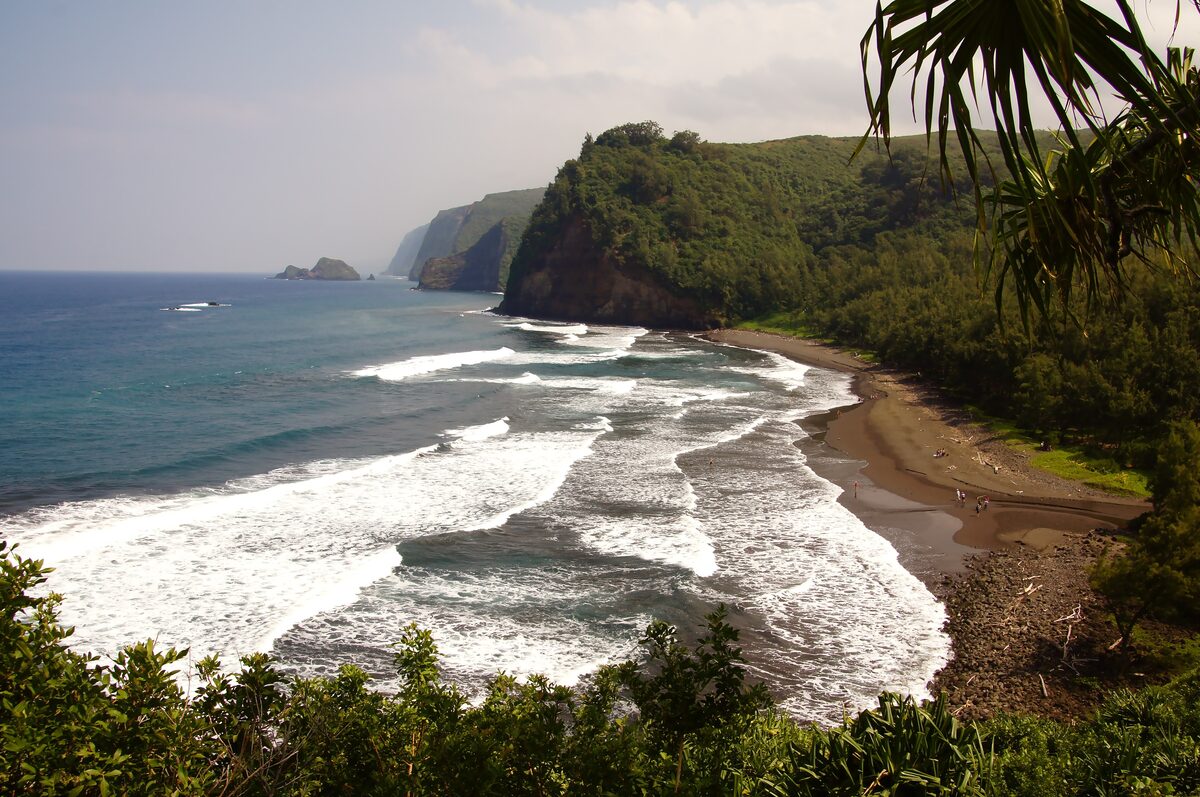 Black sand beach and surf below the green cliffs of Pololū