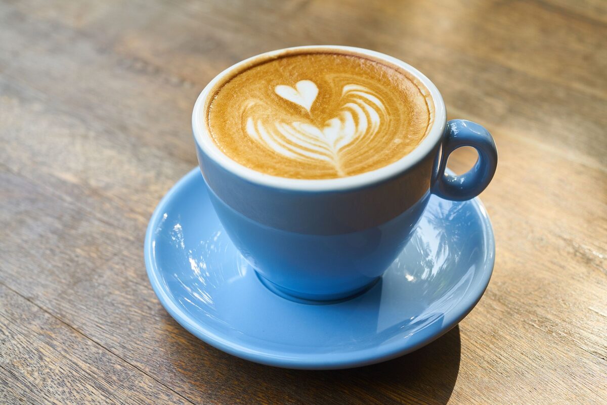 A cappuccino with heart-shaped latte art in a blue cup on a blue saucer, on a wooden table