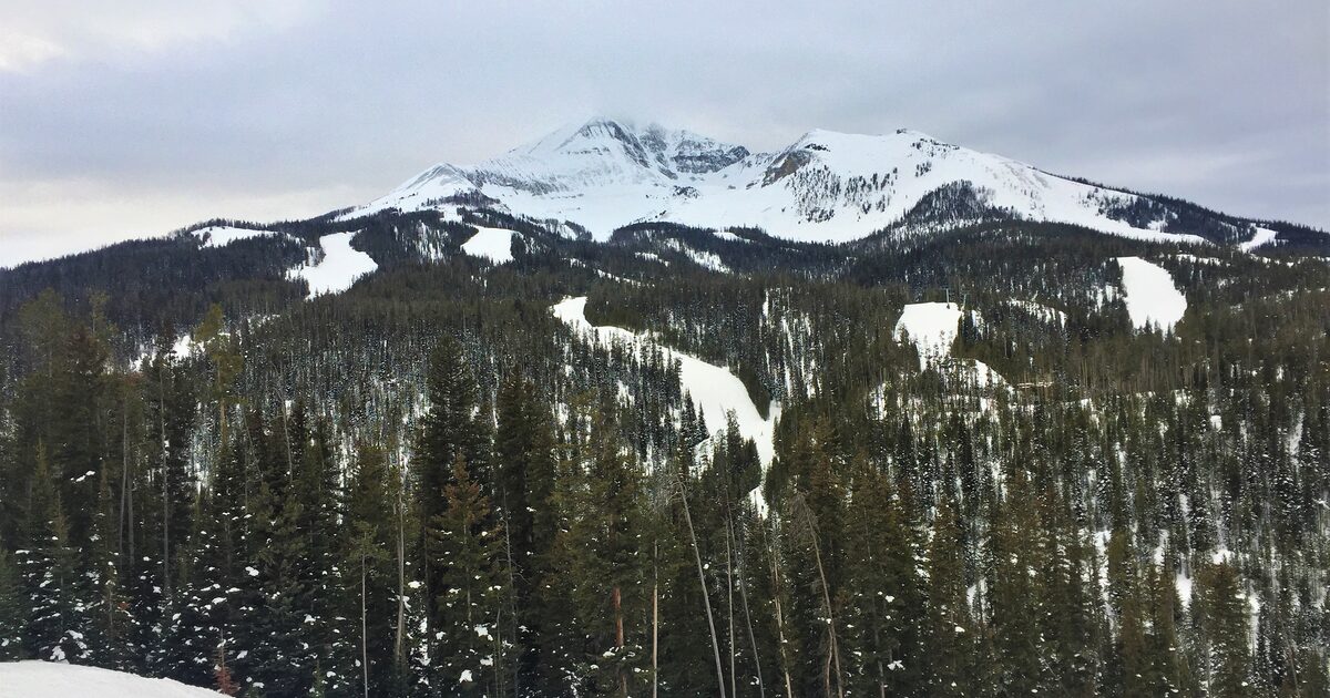 Lone Mountain above a spruce forest at Big Sky, with snow on the upper slopes and bare ground on the lower ridge