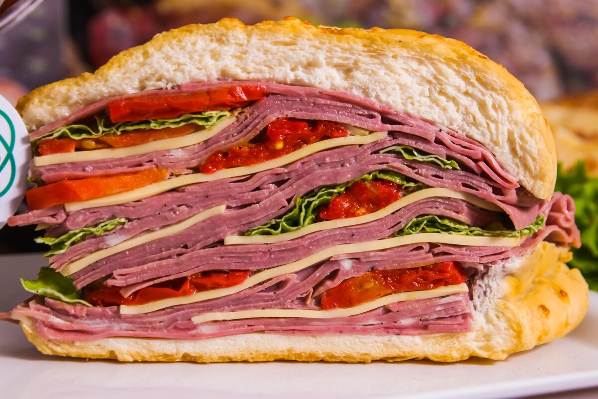 A deli sandwich cut in half, layers of sliced meat, cheese, lettuce and tomato in a thick golden roll