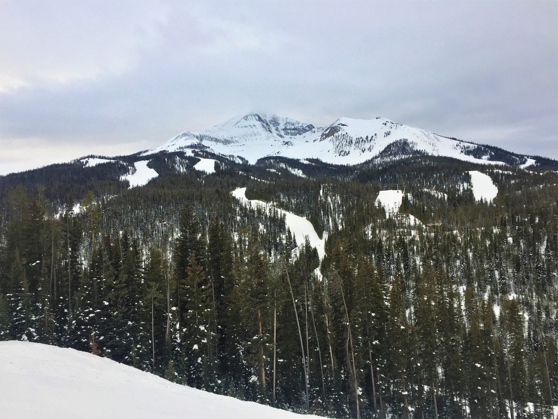 Lone Mountain above a spruce forest at Big Sky, with snow on the upper slopes and bare ground on the lower ridge
