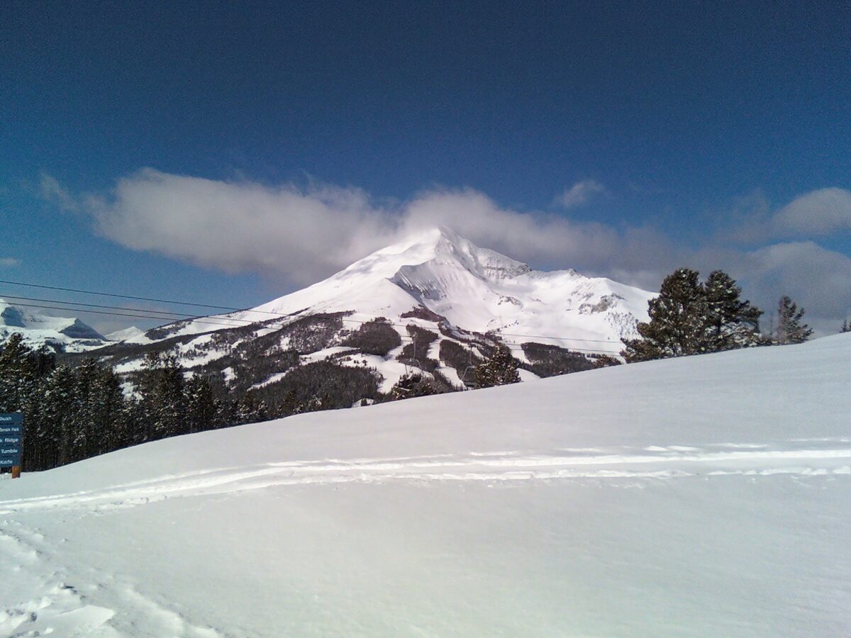 Lone Peak, the 11,166 ft summit the tram climbs, white with snow above a smooth slope and spruce, under a blue sky