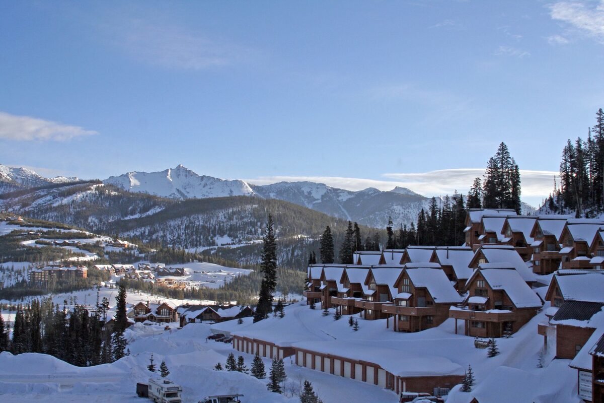 Snow-covered log lodges of the Big Sky resort village, with snowy mountain ridges rising behind them