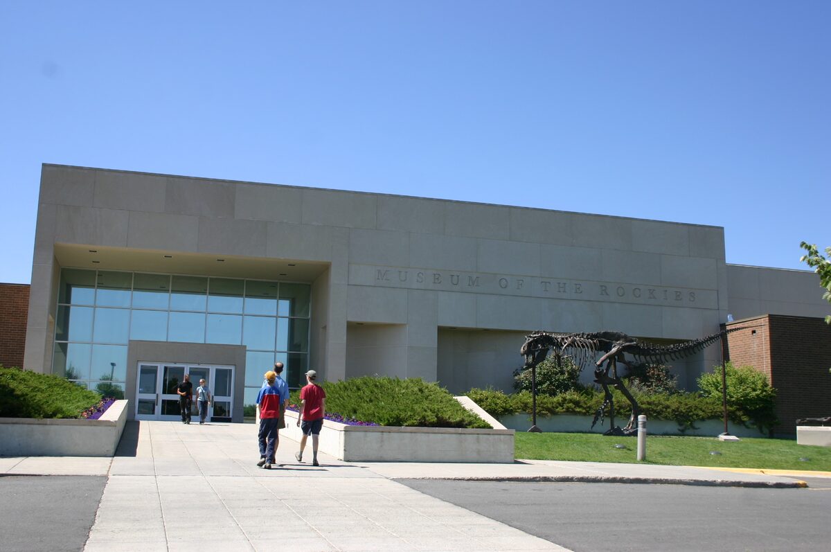 The entrance of the Museum of the Rockies in Bozeman, with a dinosaur skeleton in the garden beside it
