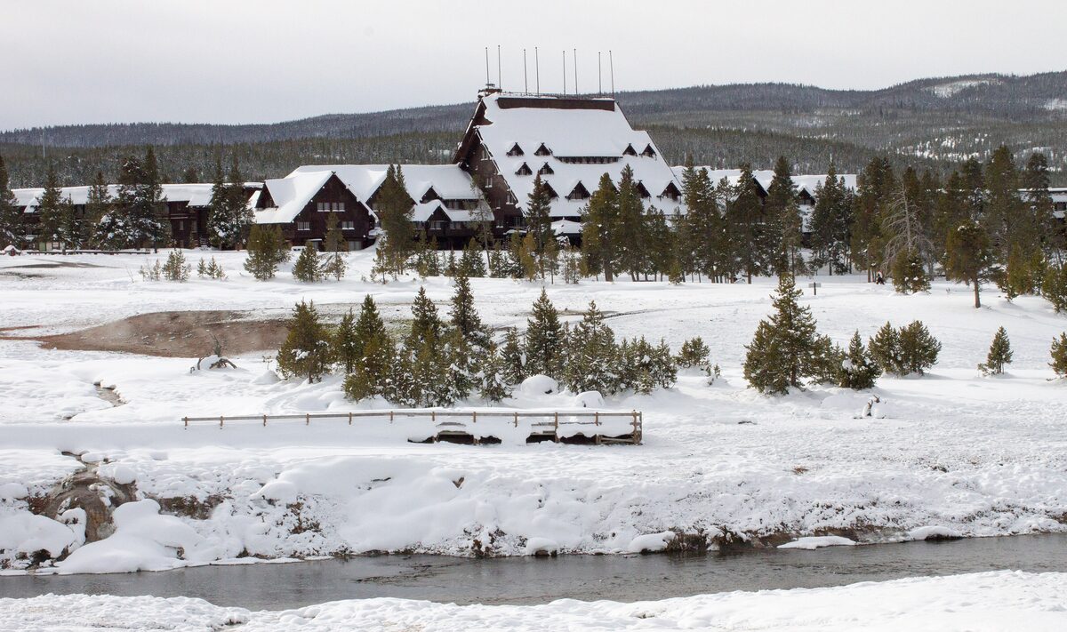 The Old Faithful Inn and lodges across a snowy field, with the Firehole River in the foreground