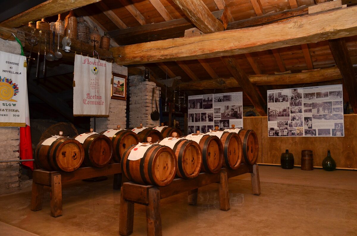 Rows of wooden barrels on racks under a timber roof, with old photographs on the walls