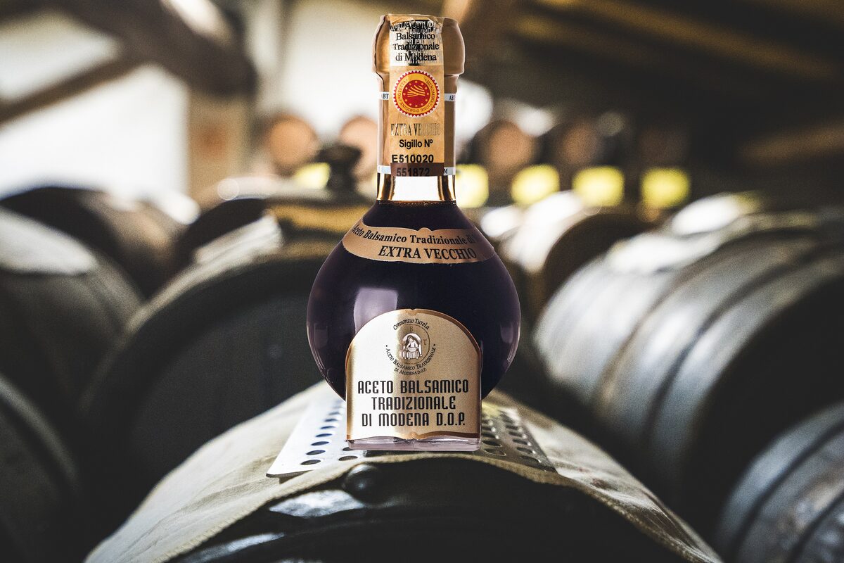 A bottle of Aceto Balsamico Tradizionale di Modena with its DOP label, in front of barrels