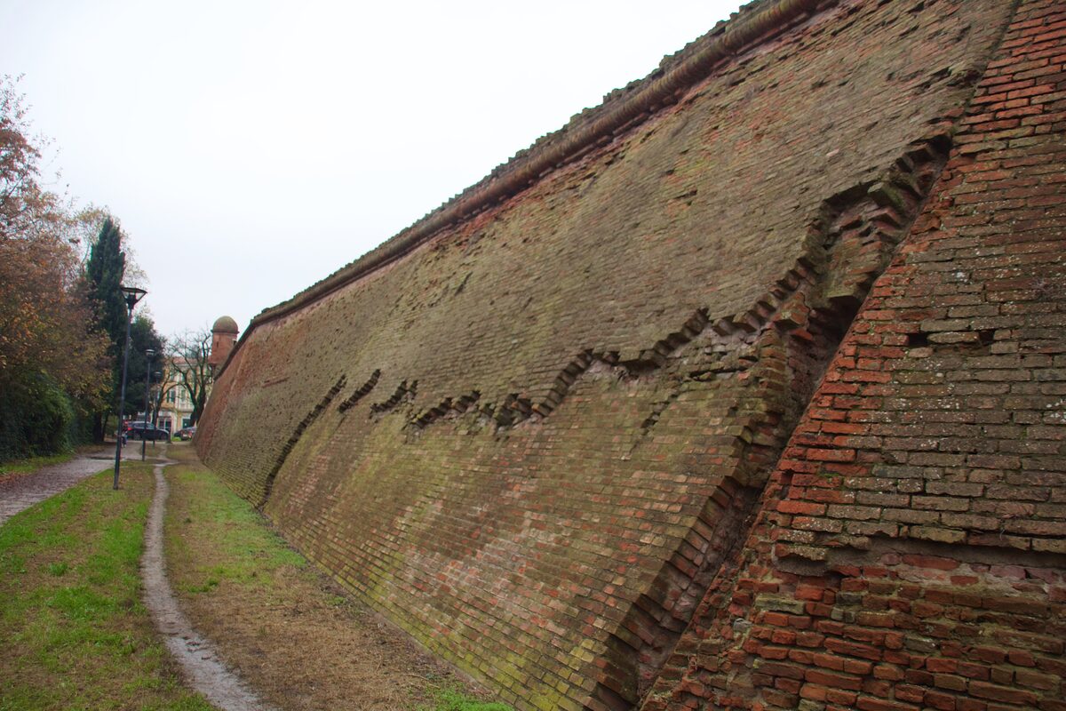 A long section of Ferrara's brick city walls with a grassy path beside them