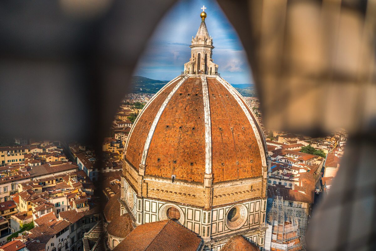 The terracotta dome of Florence Cathedral framed by an arch, with the city's roofs around it