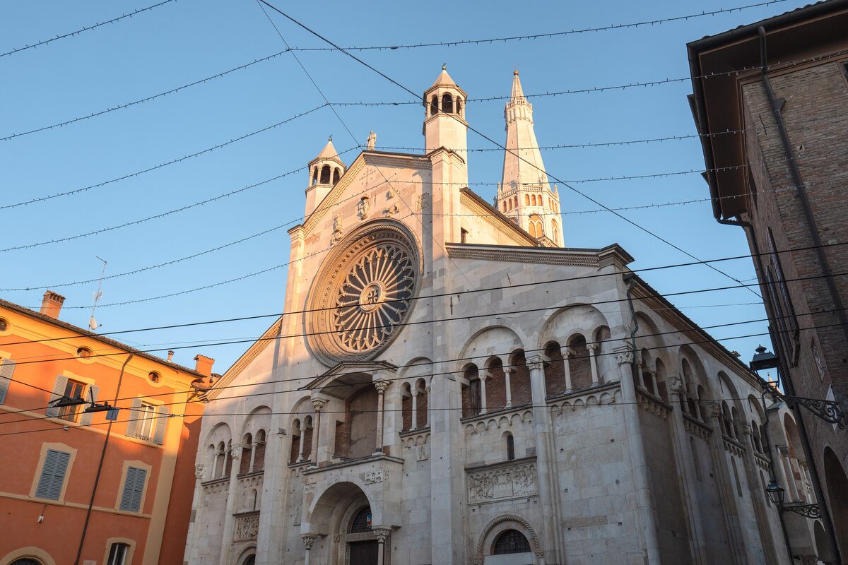 The rose window and carved Romanesque facade of Modena Cathedral, with a tower behind