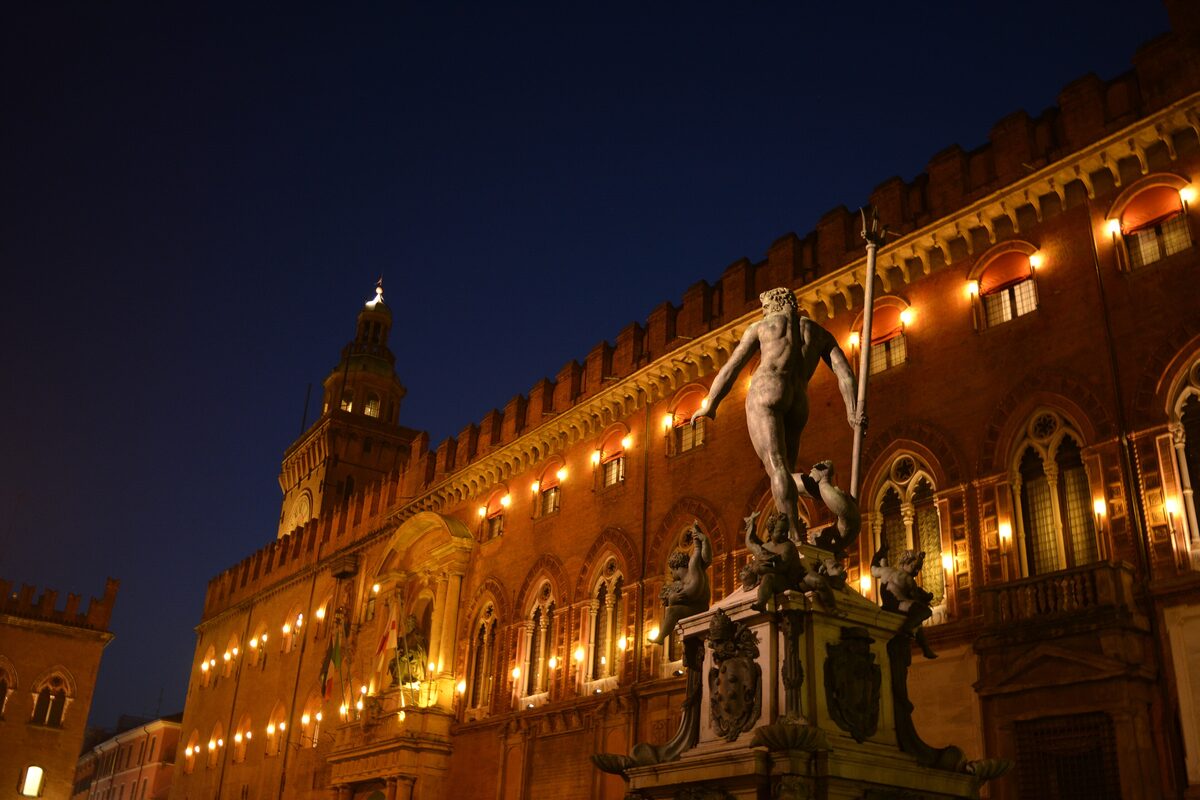 Neptune's statue on its fountain in the square at night, with the lit-up palace behind it